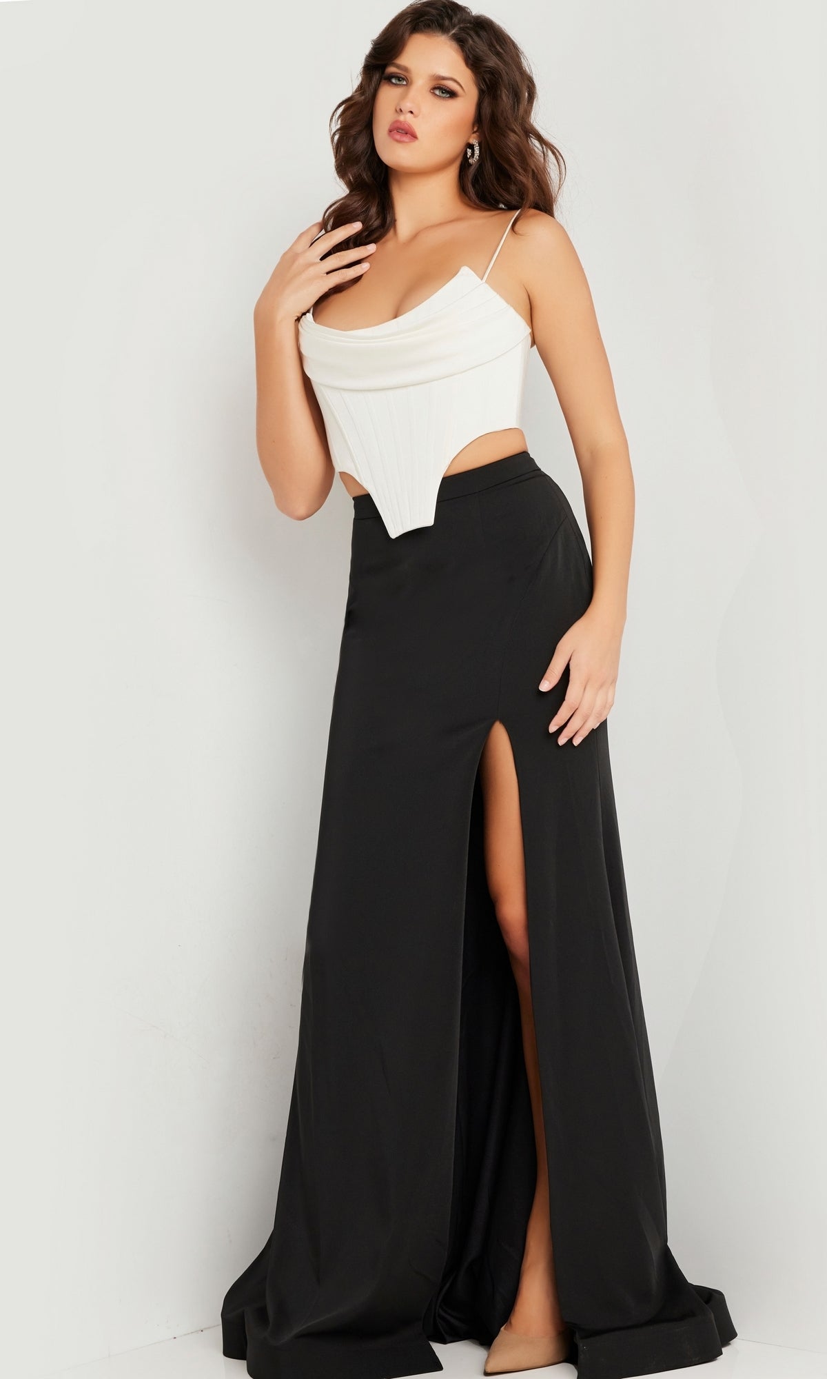 A woman modeling the Jovani Long Prom Dress 37234, a two-piece outfit with a white corset-style top and long black skirt with a high slit, stands against a plain light background.